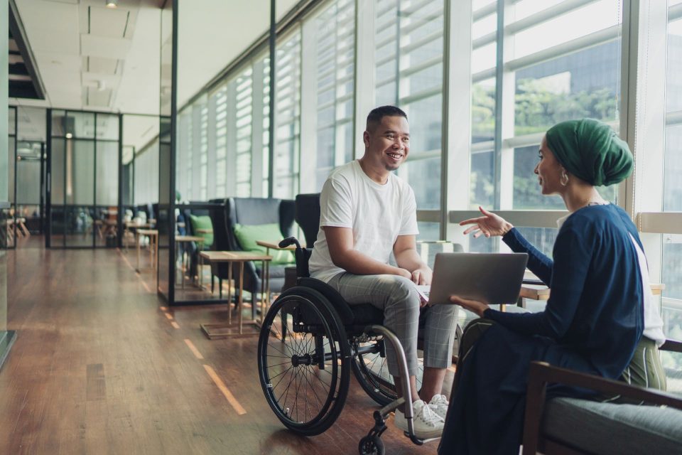 A man in a wheelchair and a woman with a head scarf in conversation