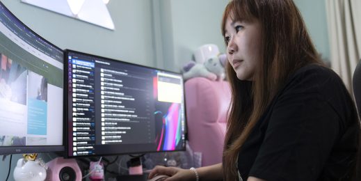 A woman sits at a desk in front of computer monitors