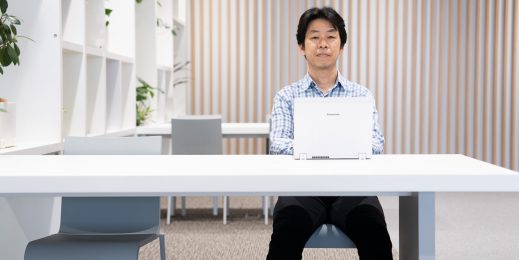 Man sitting behind a desk with a laptop on it, looking straight at the camera