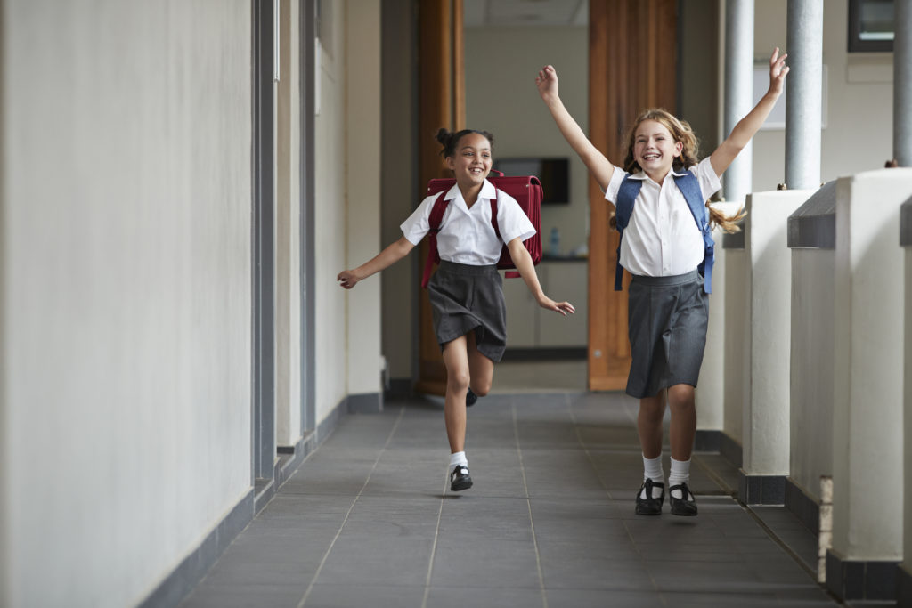 two school girls running across the hall