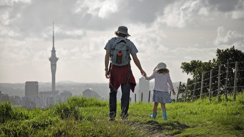 AI strengthens te reo Māori use at NZ’s largest digital news site. Image of a parent and child holding hands walking in Auckland overlooking the skytower.