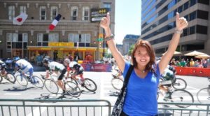 Isang stands by a roadside, celebrating as a bike race ensues behind her