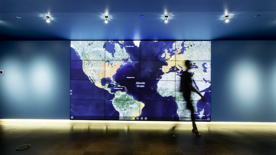 Photo of an interactive LED wall showing a map of the world, with a man walking in the foreground in front of it