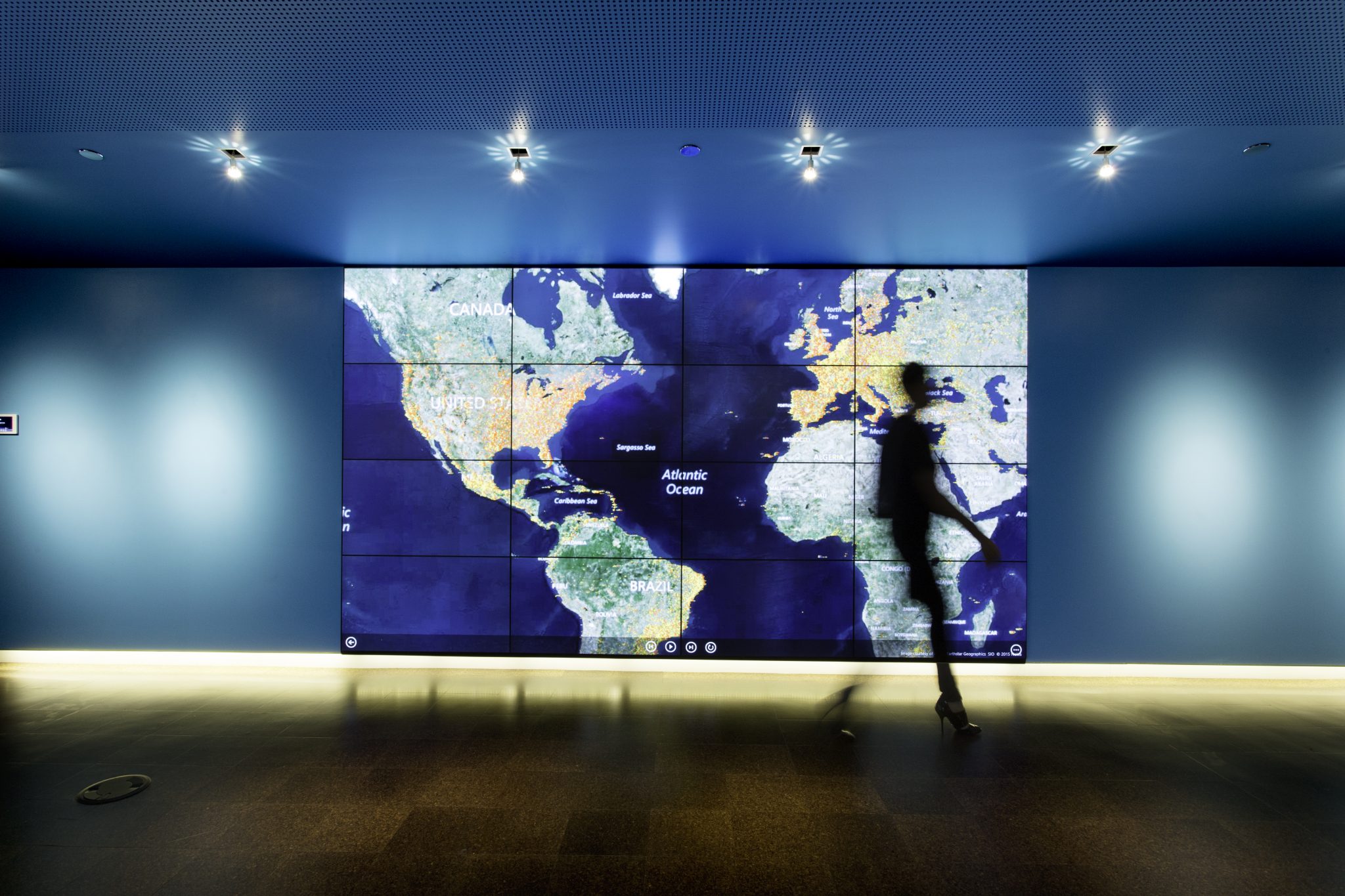 Photo of an interactive LED wall showing a map of the world, with a man walking in the foreground in front of it