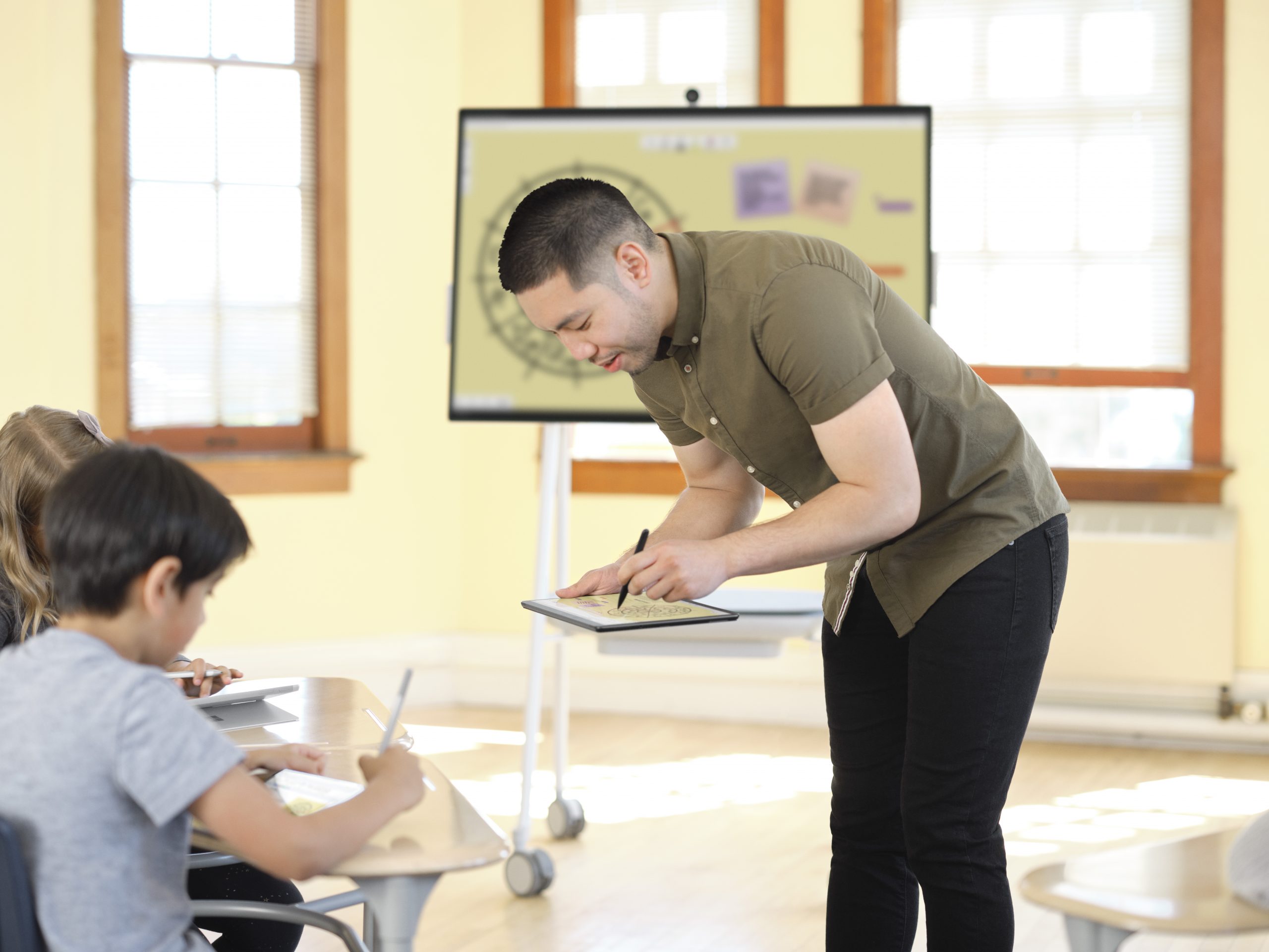 Asian male teacher instructing students inside a classroom using a Microsoft tablet