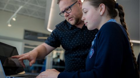 A teacher helping a student who is working with EdChat on a computer.