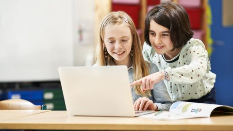 Two children looking at a computer and smiling.