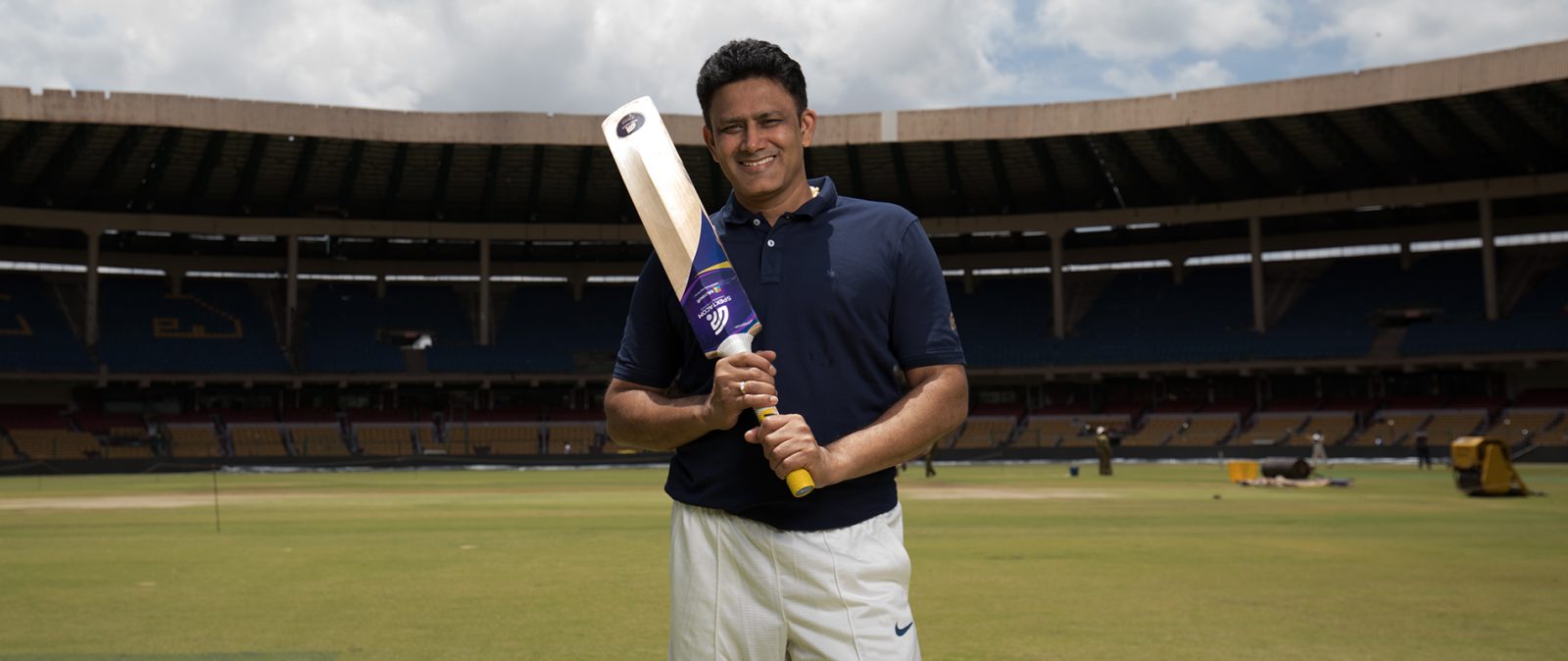 A man standing with a cricket bat inside a stadium