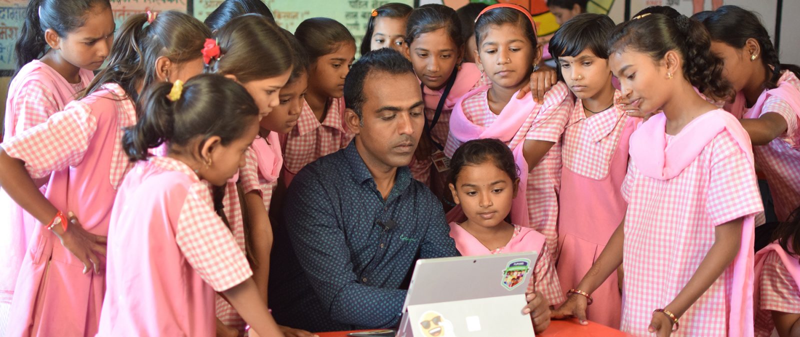 A group of children and a man huddled around a laptop