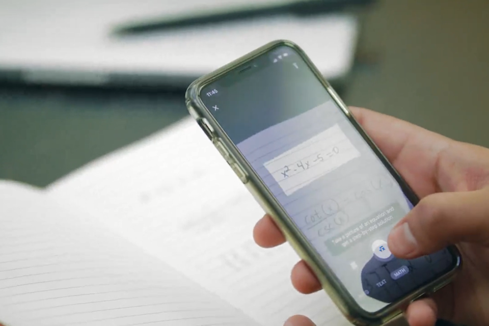 A person scanning a math problem written in notebook through Microsoft Math Solver Mobile App