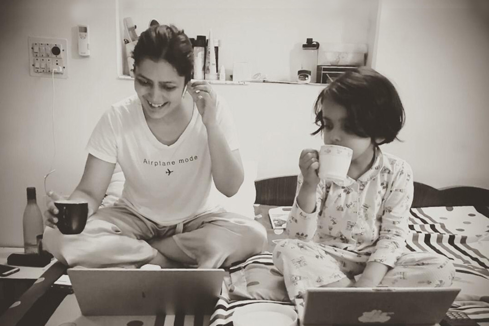 A woman working from home on her laptop, as her daughter looks on and imitates her actions on a toy laptop.