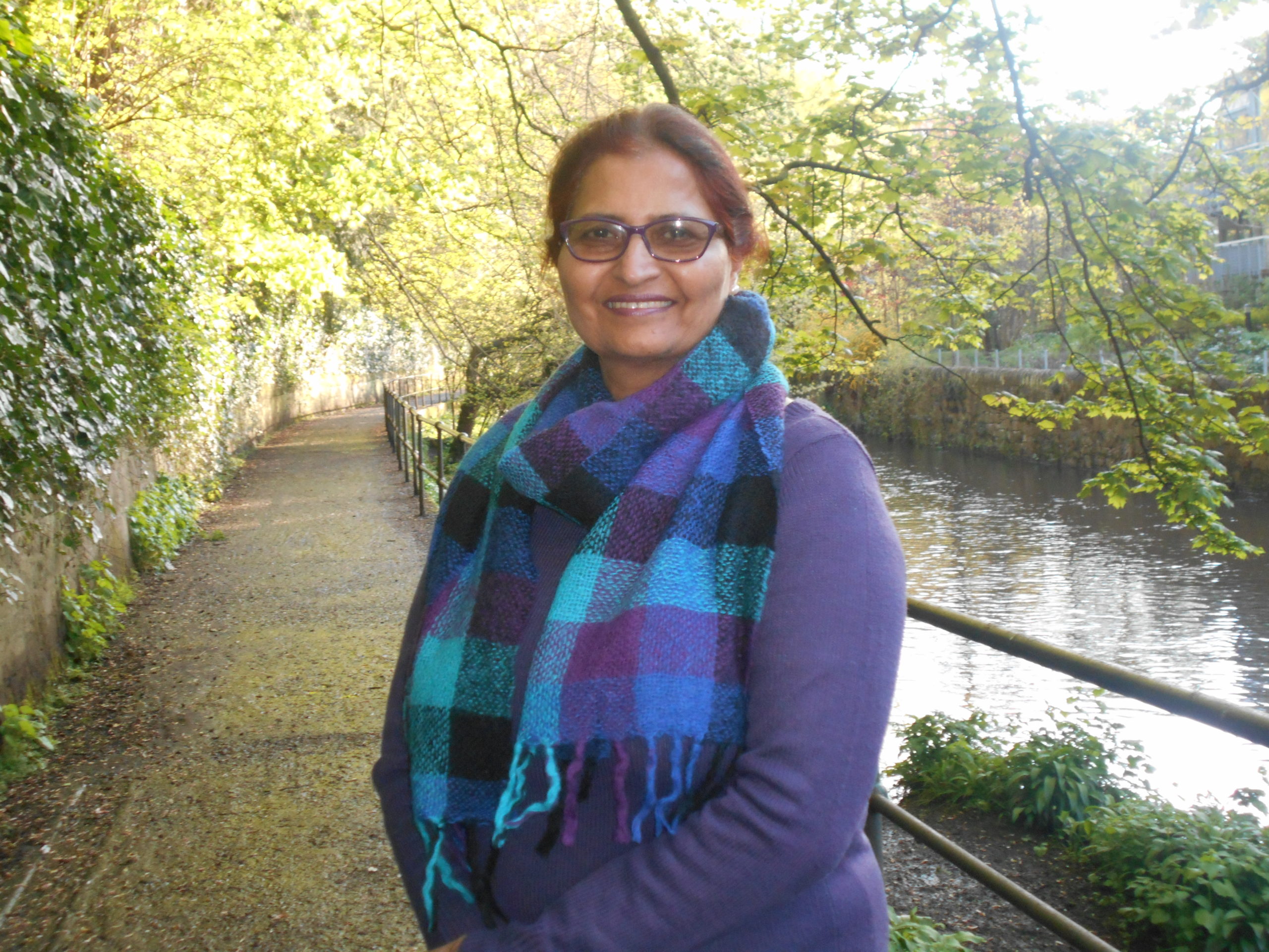 a woman smiling at the camera with a canal and foliage in the background