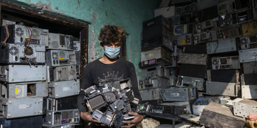 a man handling e-waste with CPU cabinets stacked in the background