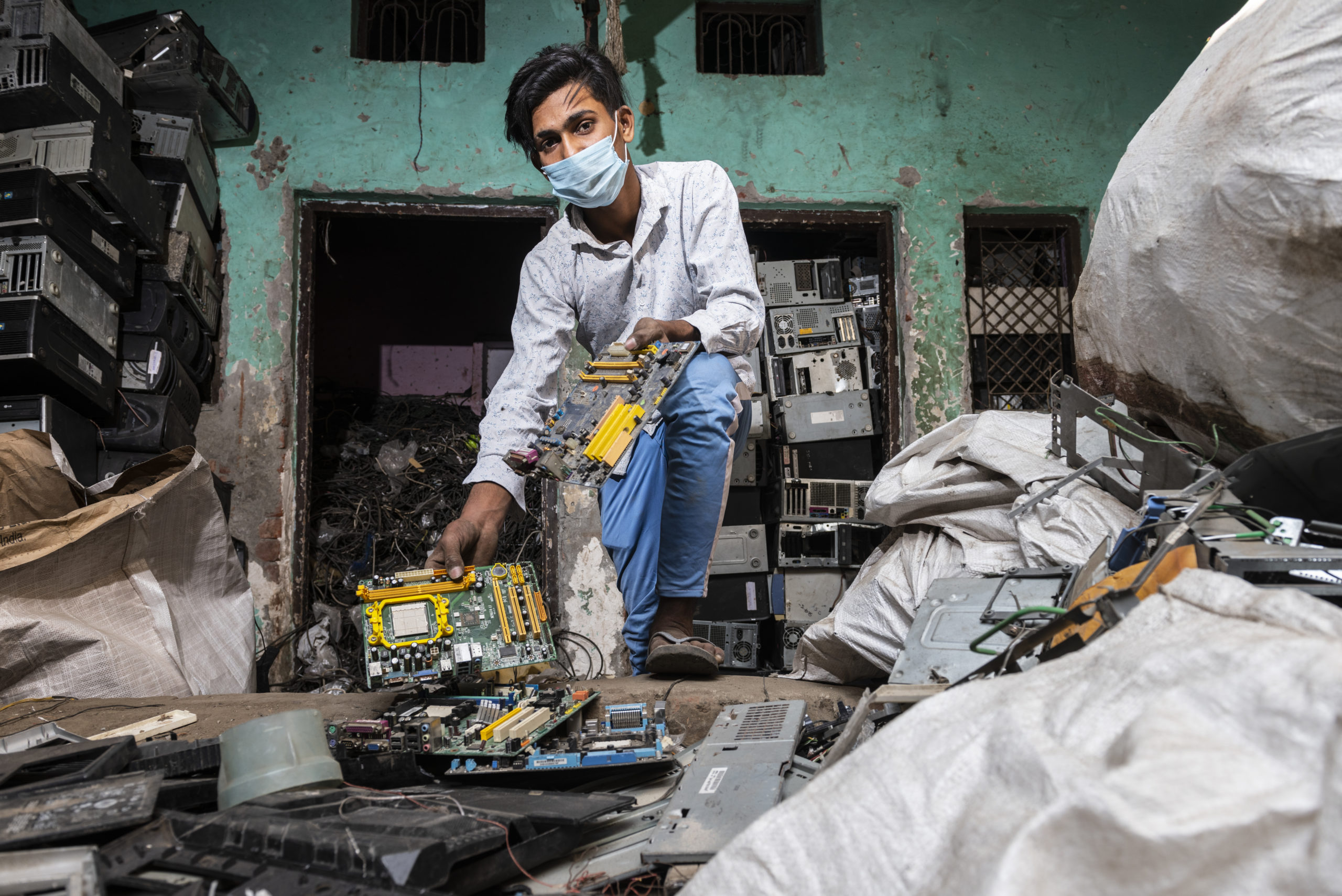a man holding a motherboard amid a pile of electronic waste