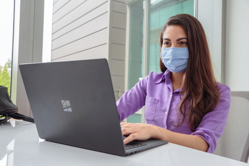 Photo of a woman wearing a mask and working on a laptop