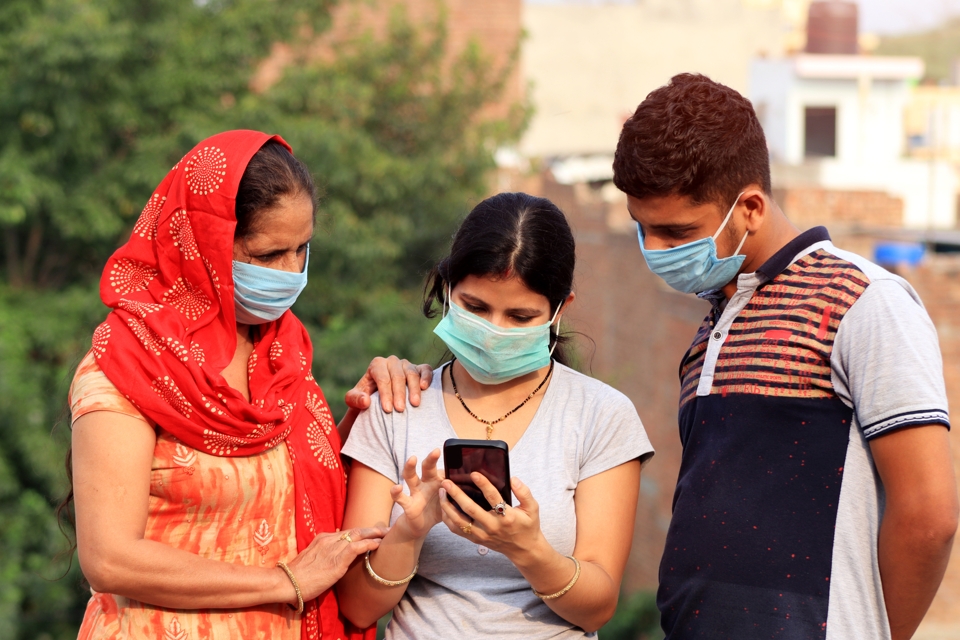 A family in rural India wearing face masks and using a mobile phone