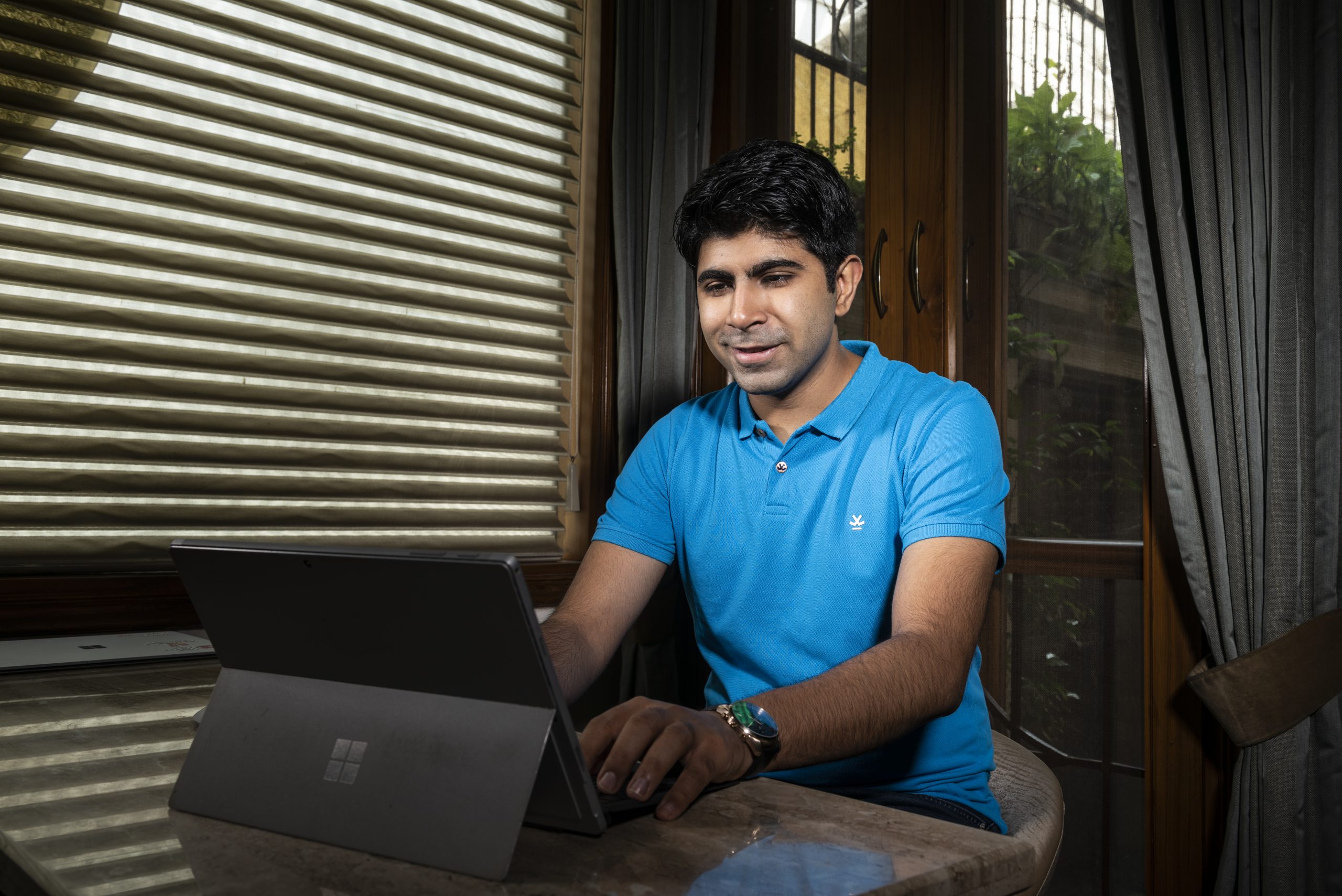 a man wearing a blue t-shirt working on a Surface Pro laptop