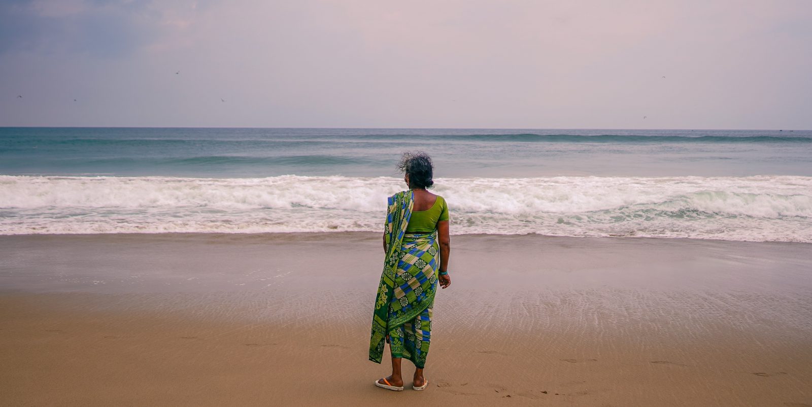 a woman wearing a green sari at a beach looking out at the sea