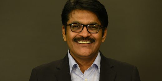 a man wearing a formal jacket and spectacles looking at the camera