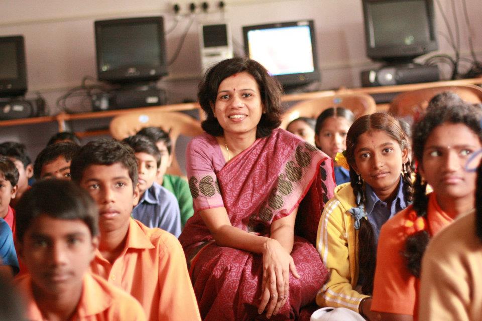 a woman wearing a sari sitting with a bunch of students