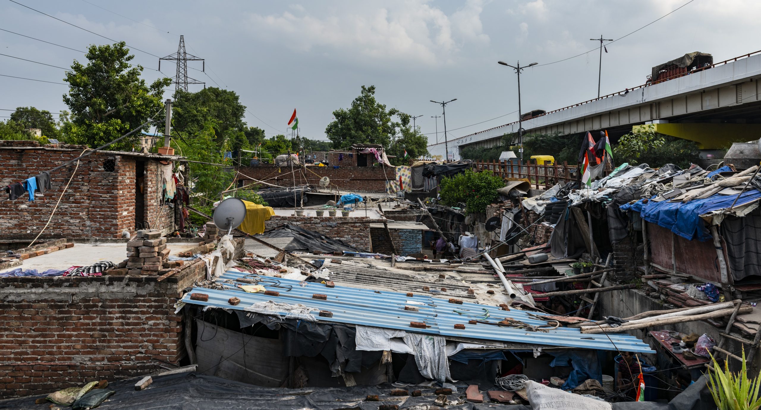 a shot of a congested urban slum with tin-roofed shacks in delhi underneath a flyover