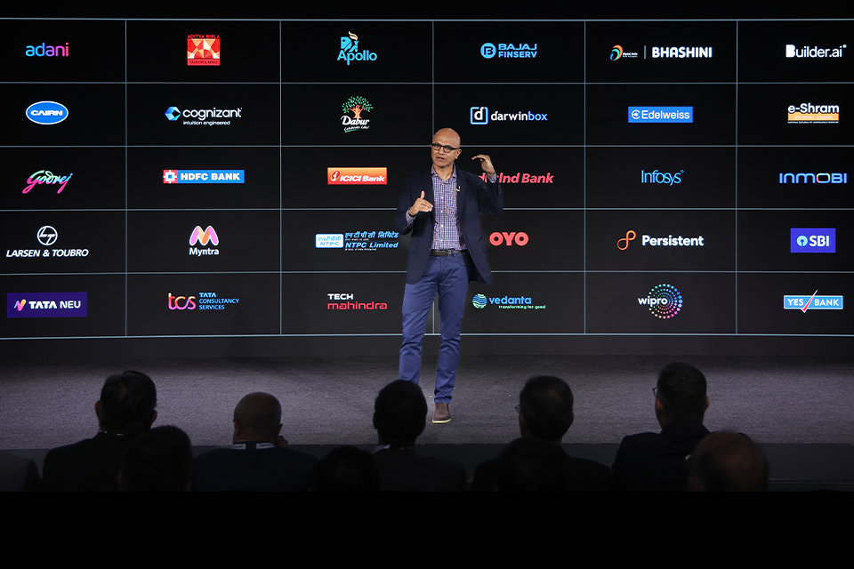 a man giving a keynote with the screen behind him displaying logos of various companies
