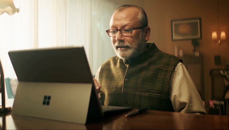 A spectacled man sitting at a desk with a laptop