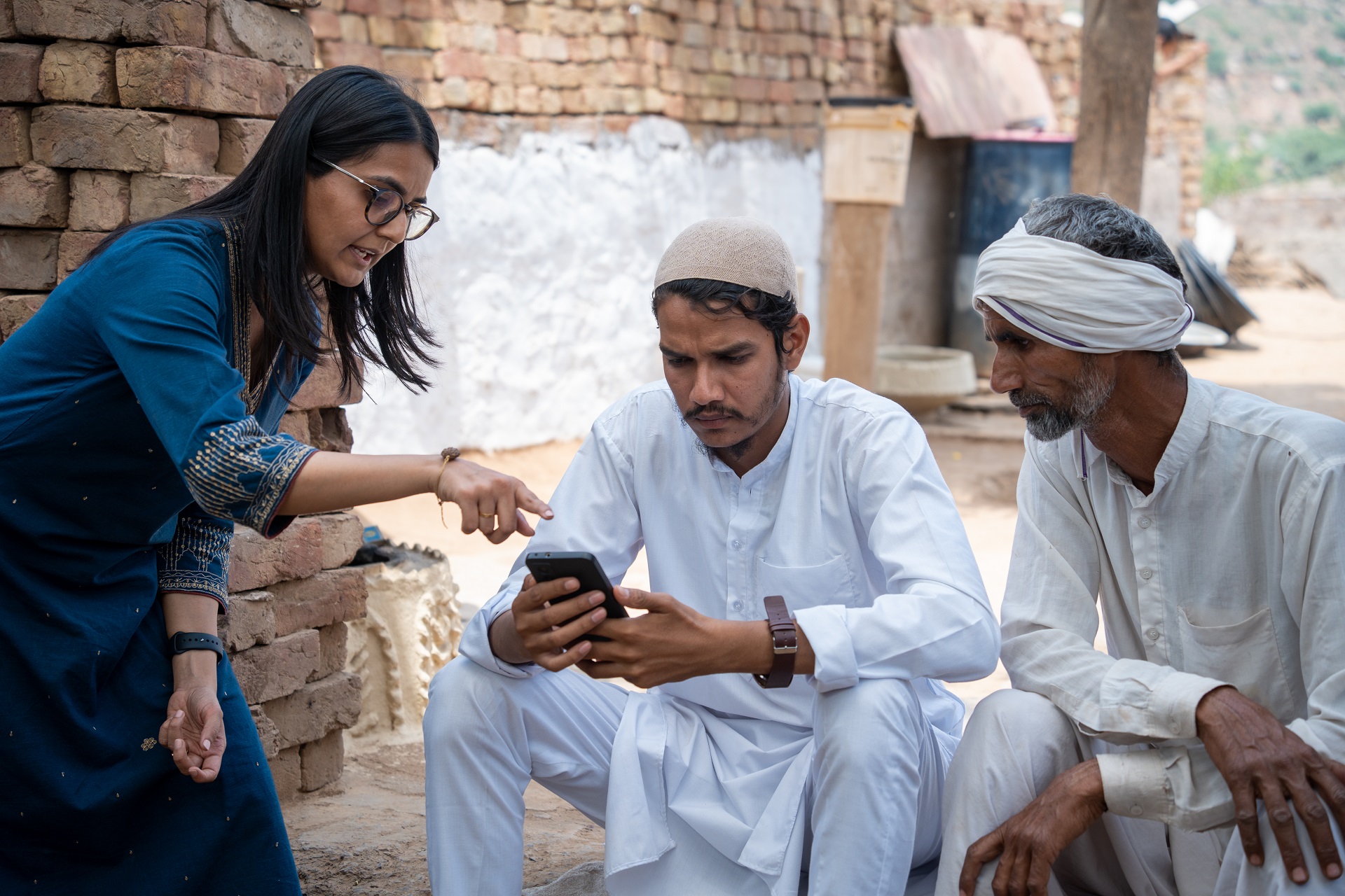 A woman helping two farmers use the Jugalbandi app on a mobile phone.