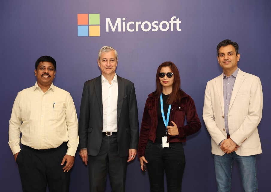 Photograph of three men and a woman against a Microsoft backdrop at the Microsoft Sustainability Hackathon