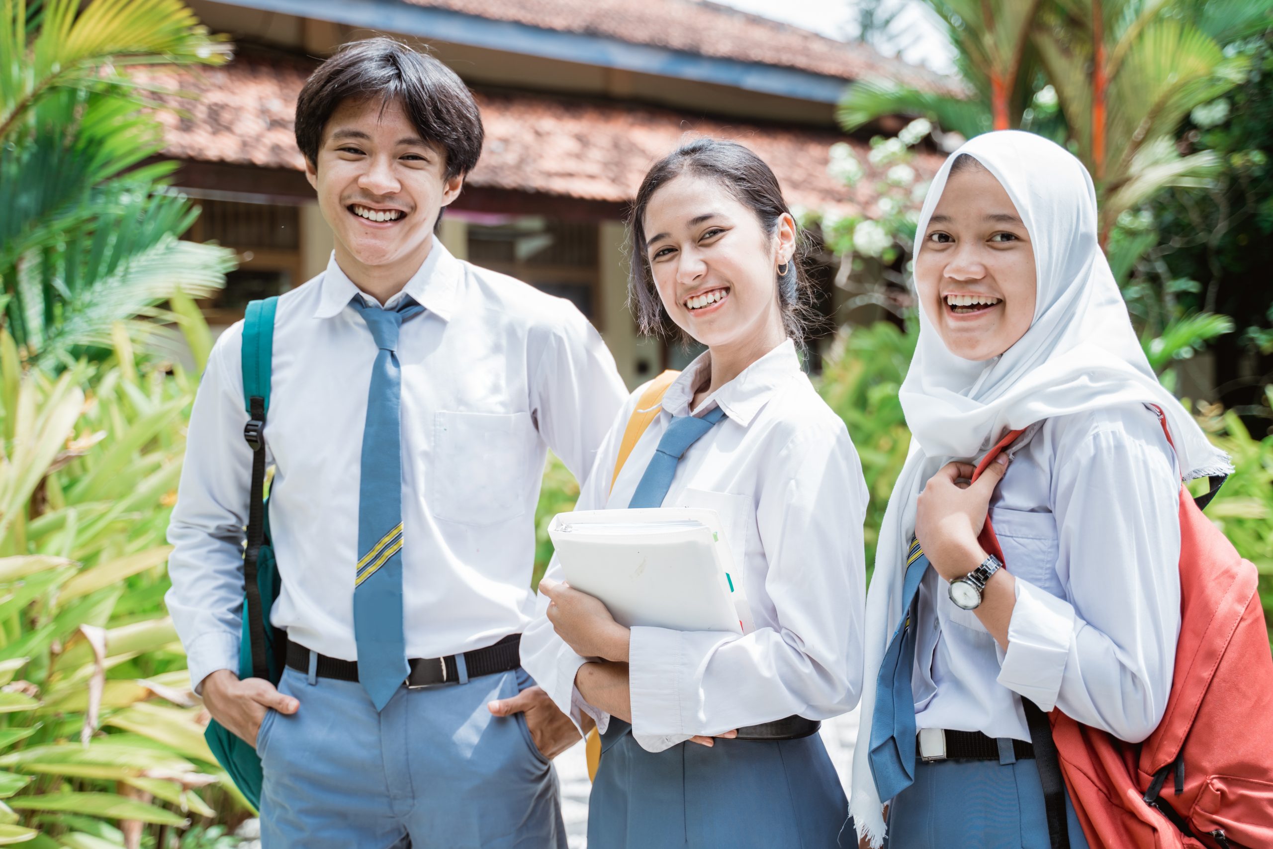 Three students in Indonesian high school uniform, each carrying a backpack, smiling