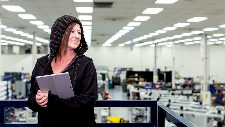 Девушка-программист с ноутбуком в руках и капюшоном на голове оглядывается в производственном помещении