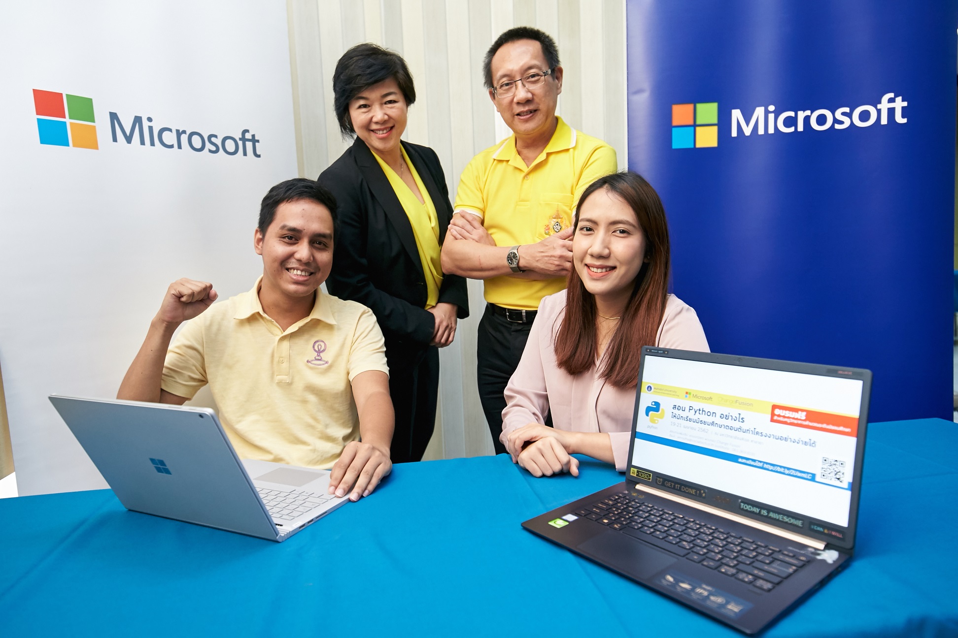 Two men and two women with two laptops in front of white and blue Microsoft signs
