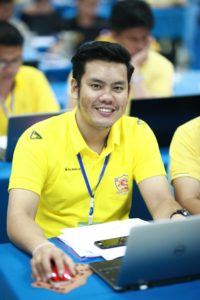 Man in yellow polo shirt smiling while using laptop