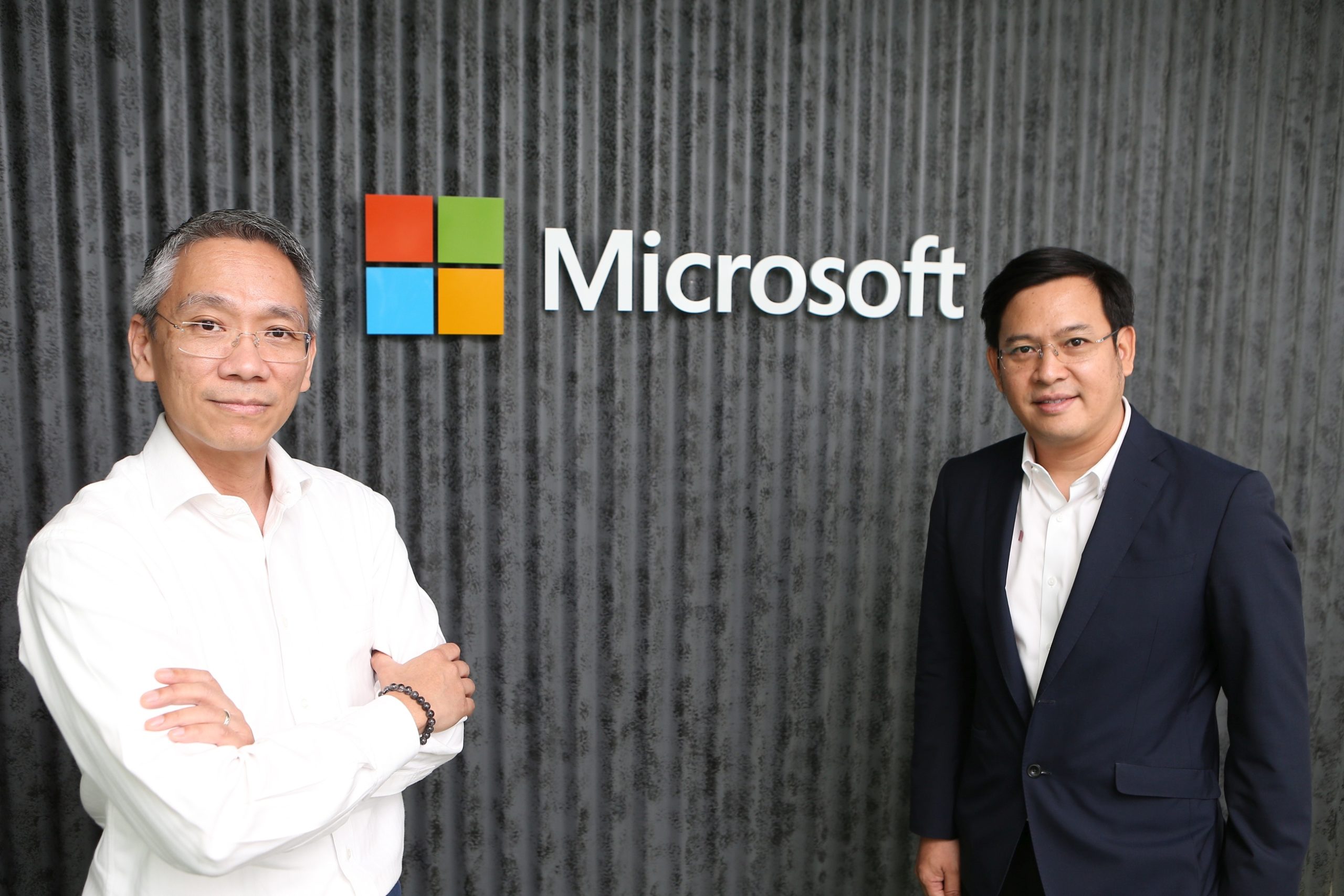 Man in white shirt and man in dark jacket in front of Microsoft logo