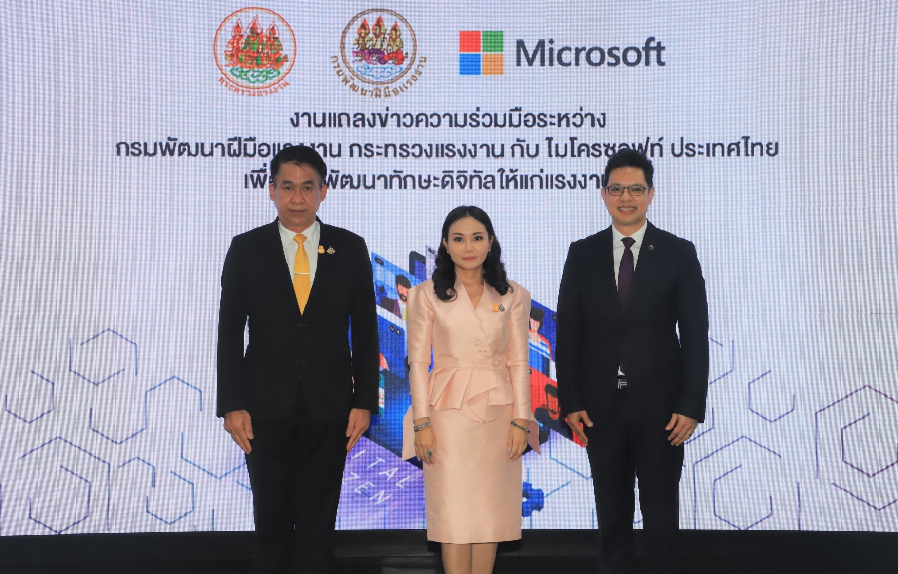 Two men and a woman in formal wear in front of LED screen
