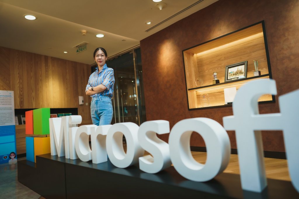 Woman in light blue shirt and pants standing behind Microsoft logo