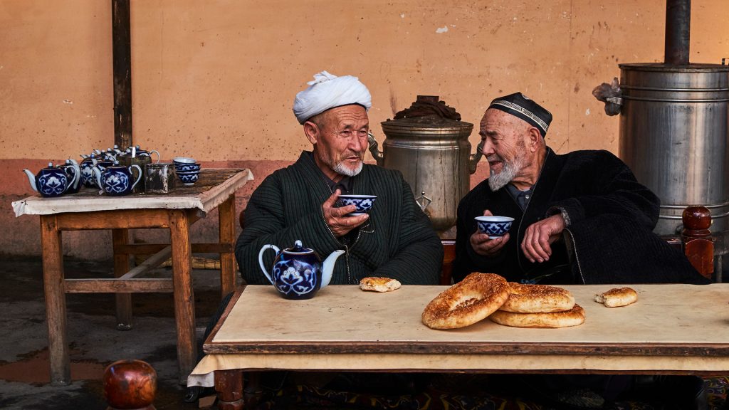 2 人の男性がウズベキスタンのフェルガナ地方にある伝統的な茶室「チャイカーナ」でお茶を飲んでいます。