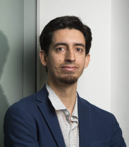 Microsoft senior researcher Nicolas Villar in a blue jacket stands against a glass wall, looking into the camera
