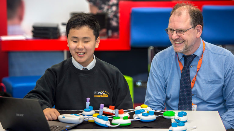 Daniel sits at a desk with Jonathan Fogg, both smiling in front of Code Jumper pods