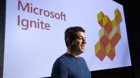 Rohan Kumar, corporate vice president for Azure Data, stands in front of a screen with the words “Microsoft Ignite”