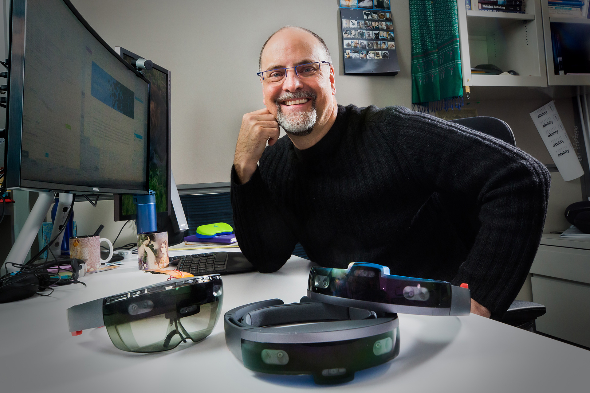 Microsoft researcher Ed Cutrell in his office with HoloLens devices sitting in front of him on his desk