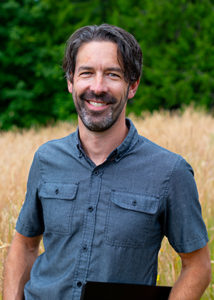 Brian Janous stands smiling in a field