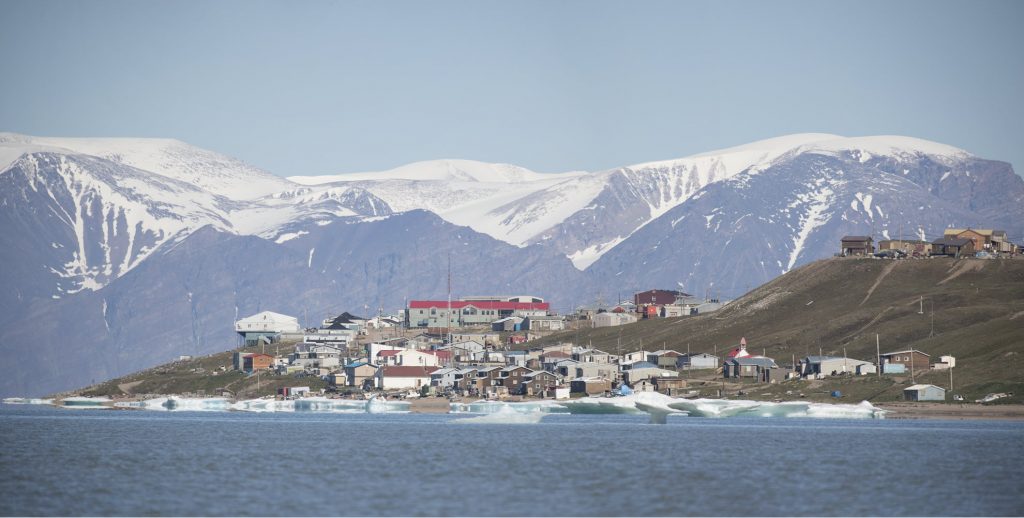 Buildings and houses on the shore of a fjord in Pond Inlet on Baffin Island in Nunavut, Canada. The Government of Nunavut is using Windows 365 and the Microsoft Cloud to provide healthcare, education, housing and family, financial and other services to the community.