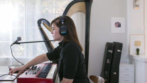Woman with headphones on plays keyboard. Harp in the background.