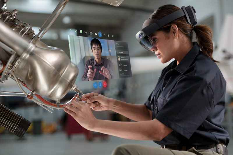 A woman communicates remotely with a colleague via hologram while working on machinery