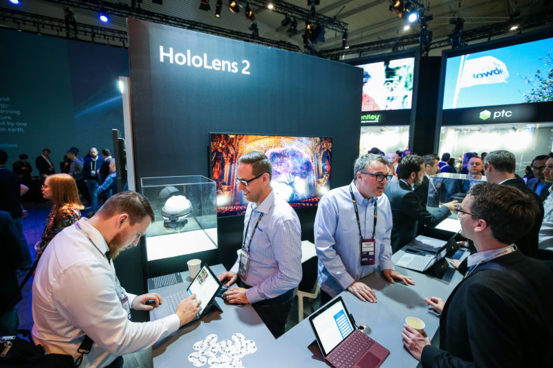 Alt: A crowd of people, some using laptops, fill a HoloLens 2 section of the Microsoft booth