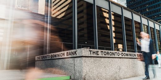 Exterior shot with blurred figure walking on city sidewalk in front of Toronto Dominion Bank concrete sign at entryway