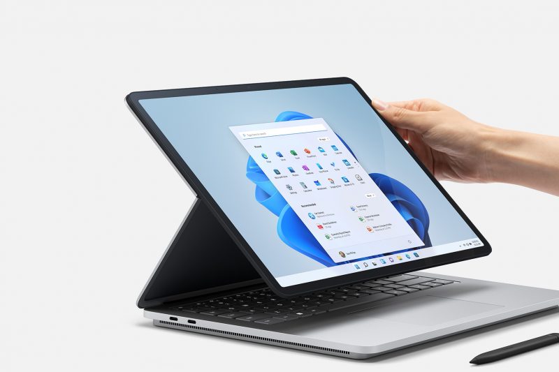 A hand touching a Surface laptop next to a Surface pen