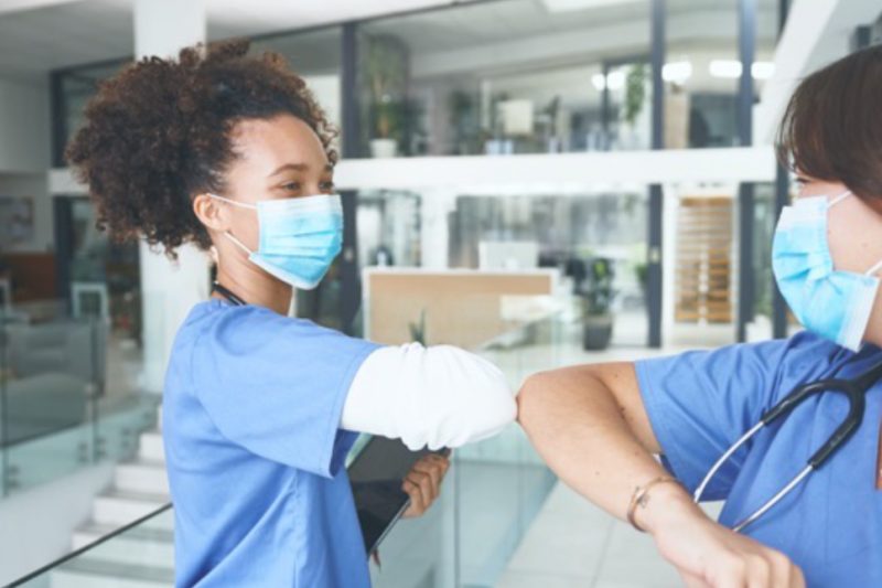 Two healthcare workers with masks on touch elbows