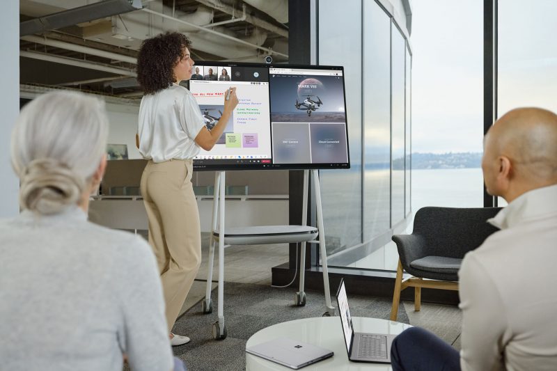 A presenter takes notes on a digital whiteboard on a Surface Hub 2S while collaborating with in-person and remote teammates.